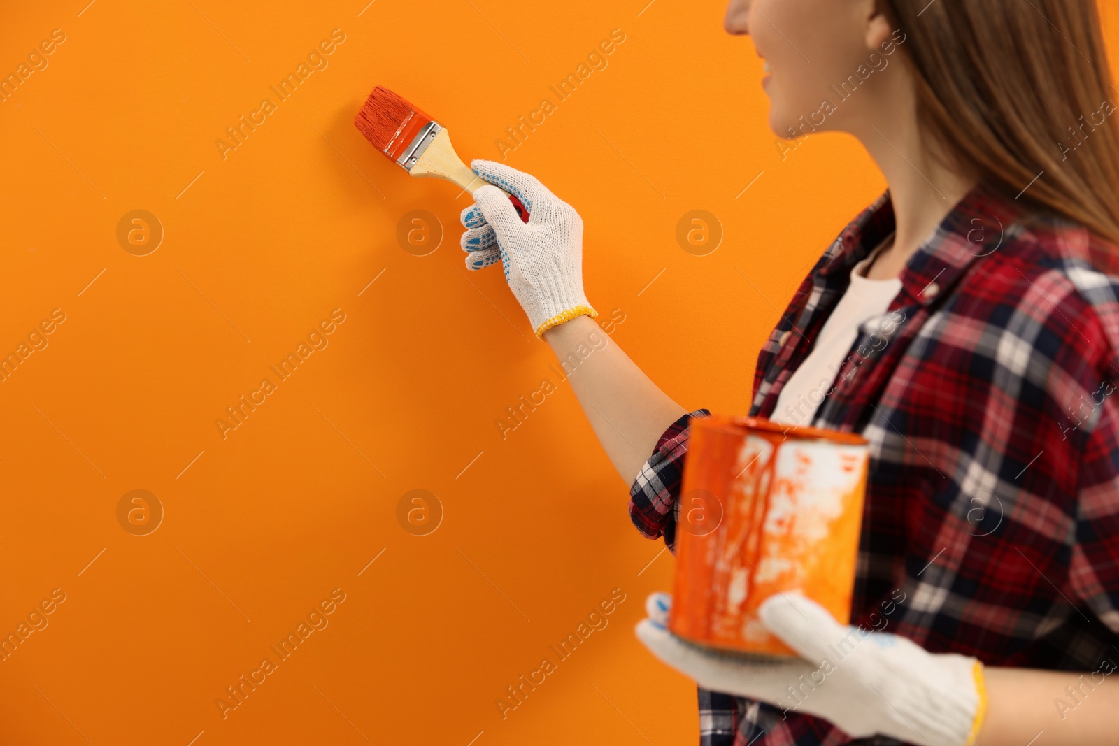 Photo of Designer painting orange wall with brush, closeup