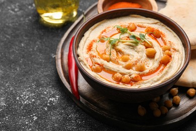 Photo of Delicious hummus with chickpeas and different ingredients on grey textured table. Space for text