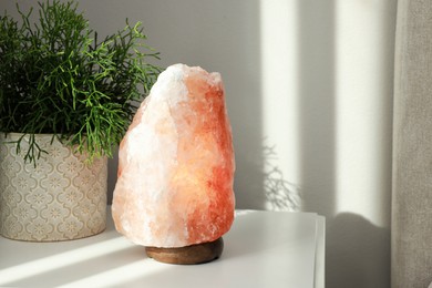 Beautiful Himalayan salt lamp and green houseplant on white table in room, space for text