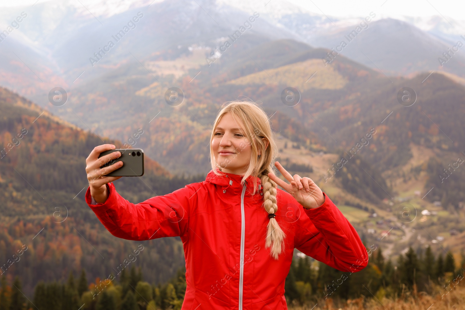 Photo of Happy young woman taking selfie with phone in mountains