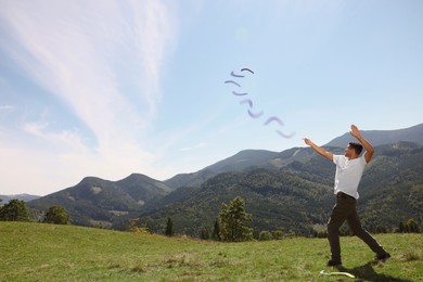 Image of Man throwing boomerang in mountains on sunny day. Space for text