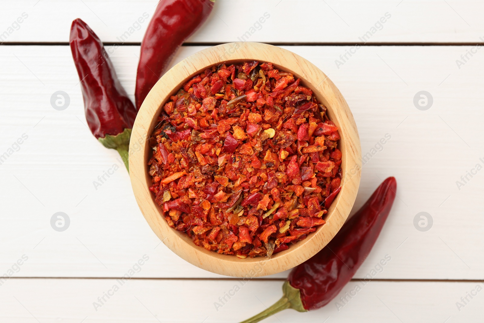 Photo of Chili pepper flakes in bowl and pods on white wooden table, flat lay