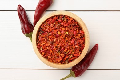 Photo of Chili pepper flakes in bowl and pods on white wooden table, flat lay