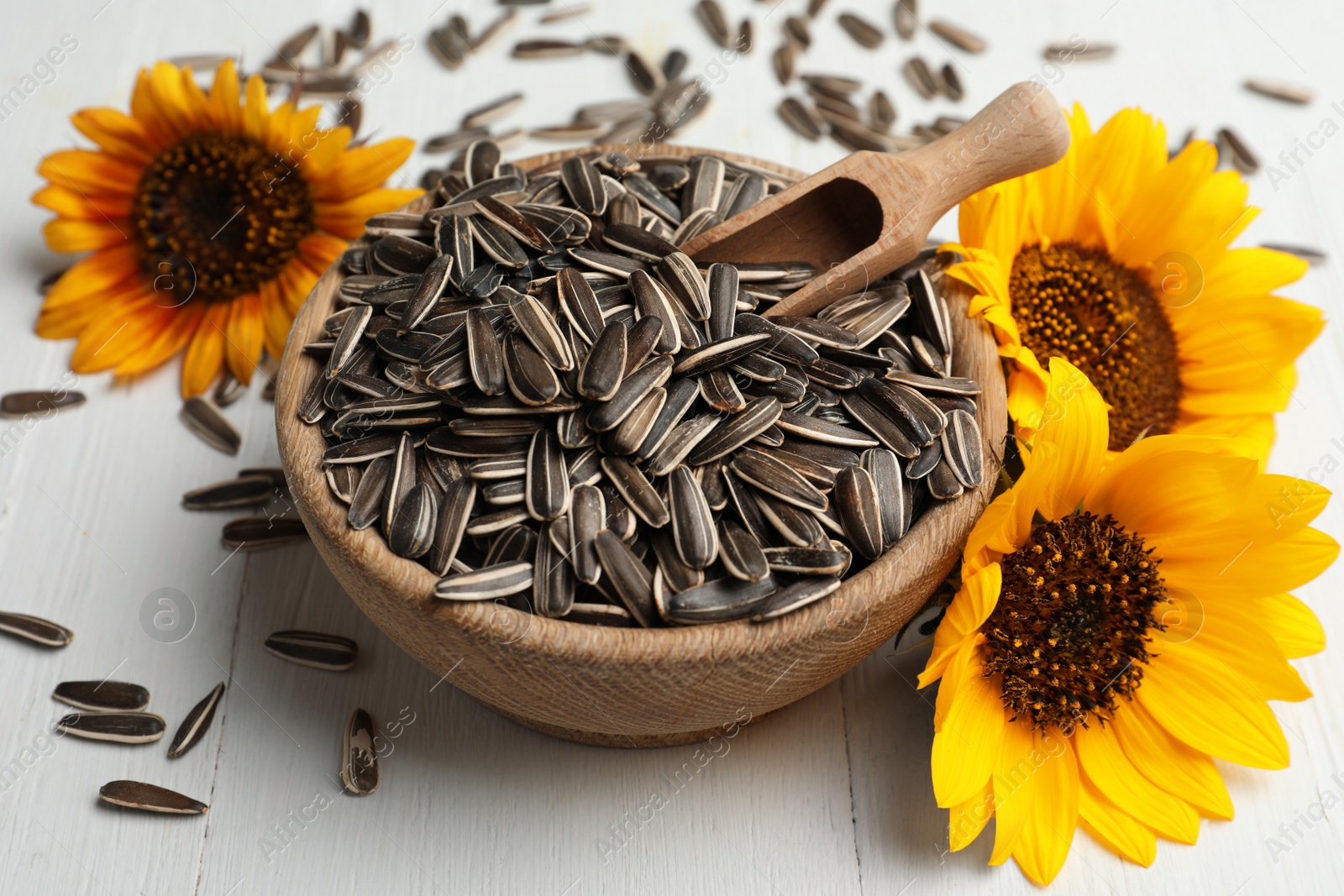 Photo of Raw sunflower seeds and flowers on white wooden table