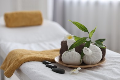 Spa stones, flowers, towel and herbal bags on massage table indoors