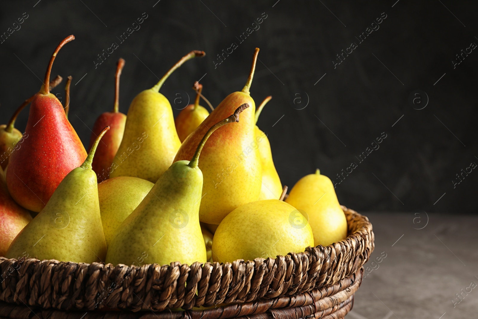 Photo of Wicker bowl with ripe pears on table against dark background, closeup