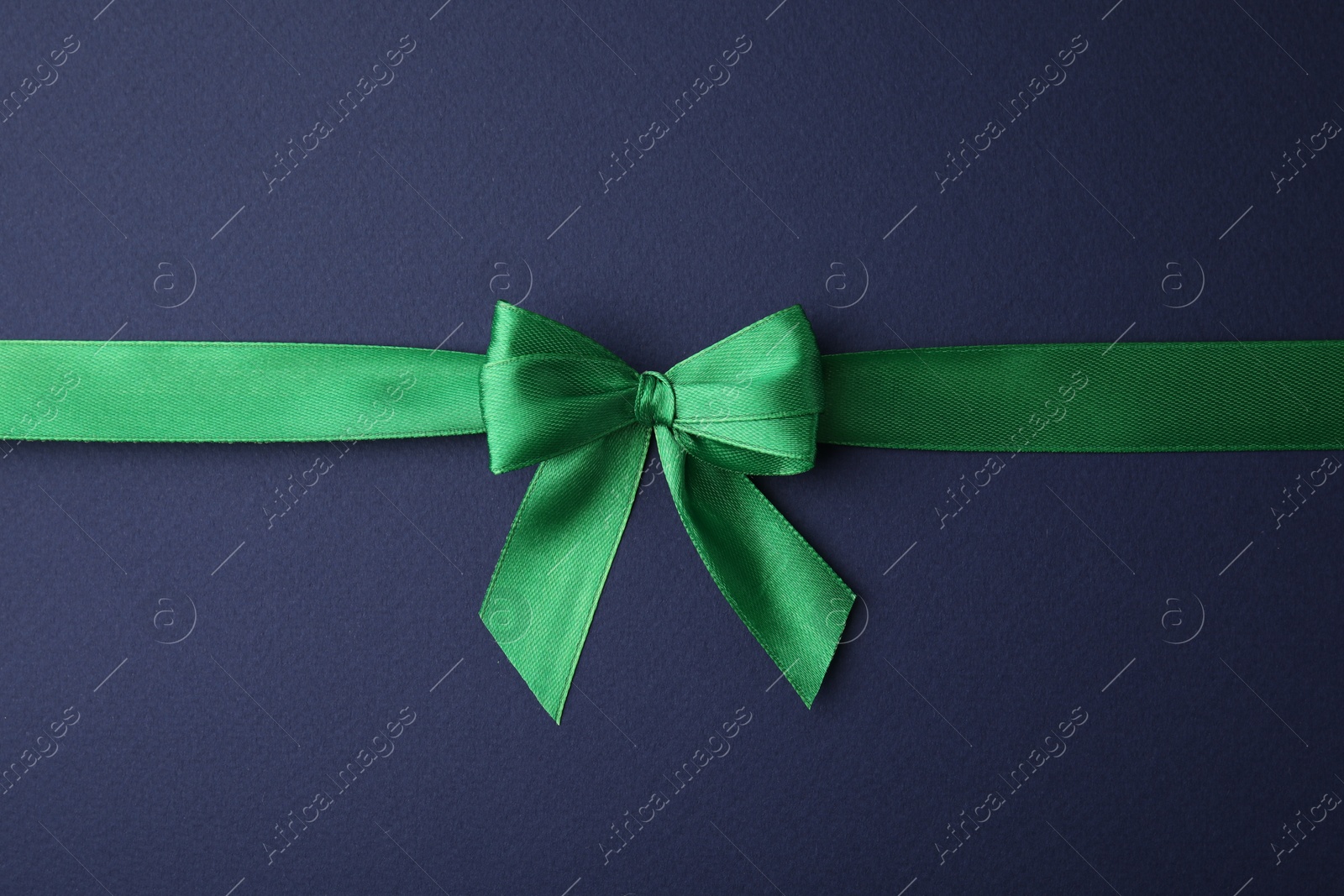 Photo of Green satin ribbon with bow on blue background, top view