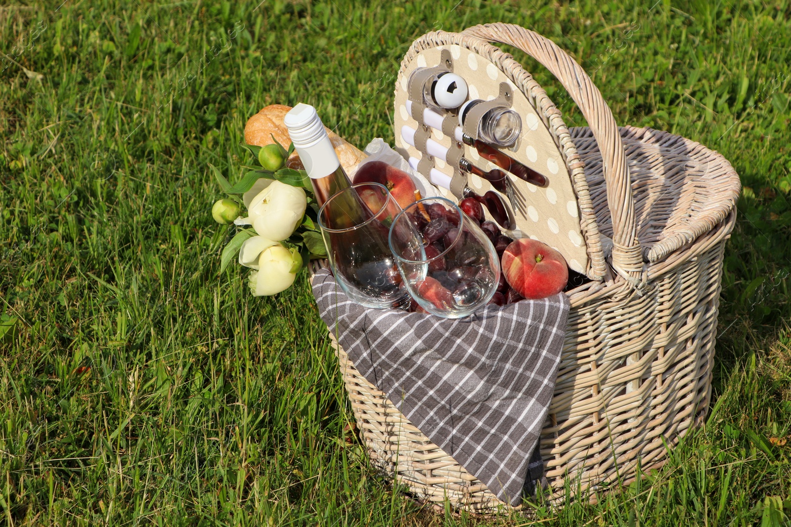 Photo of Picnic basket with tasty food, flowers and cider on grass