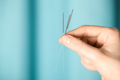 Photo of Woman holding acupuncture needles on color background, closeup. Space for text