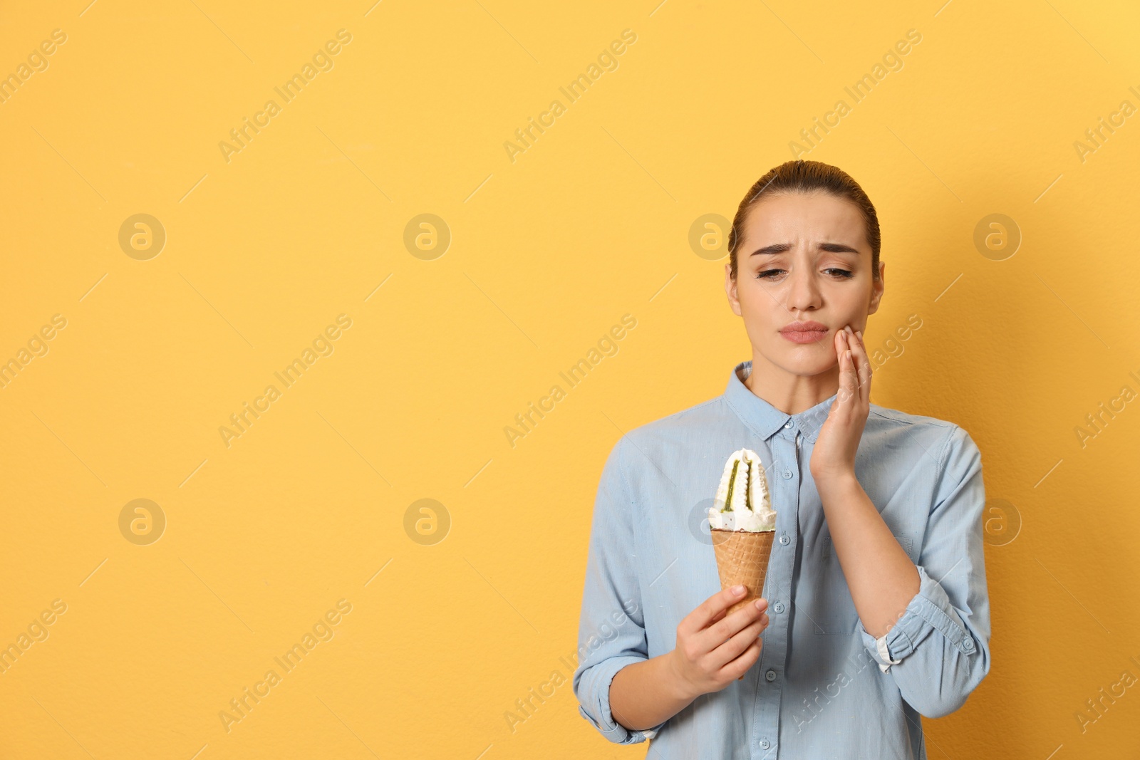 Photo of Emotional young woman with sensitive teeth and ice cream on color background. Space for text