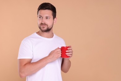 Man holding red mug on beige background. Space for text