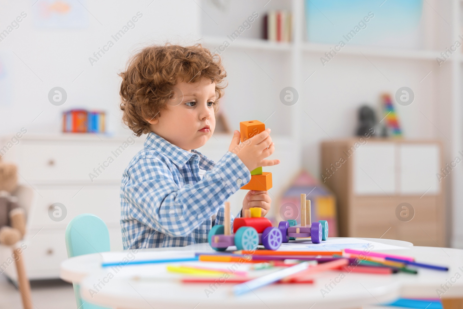 Photo of Cute little boy playing with wooden toys at white table in kindergarten