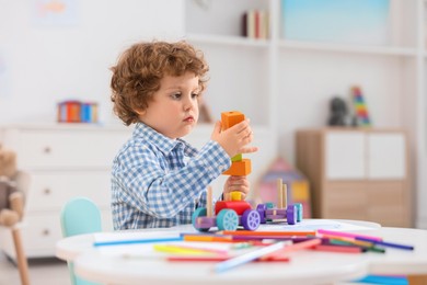 Cute little boy playing with wooden toys at white table in kindergarten