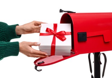 Woman putting Christmas gift into mailbox on white background, closeup. Sending present by mail