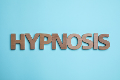 Word HYPNOSIS made with wooden letters on light blue background, flat lay