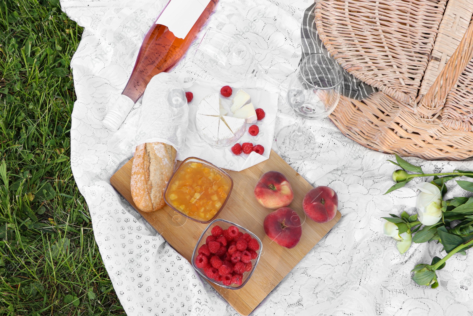 Photo of Picnic blanket with tasty food, flowers, basket and cider on green grass outdoors, flat lay