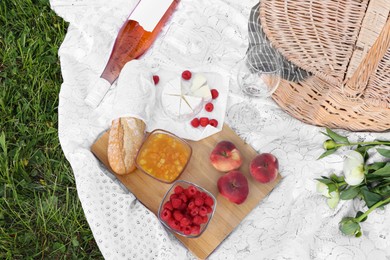 Photo of Picnic blanket with tasty food, flowers, basket and cider on green grass outdoors, flat lay