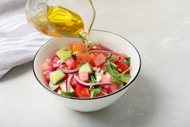 Photo of Adding olive oil to delicious salad with watermelon, vegetables and feta cheese at light table