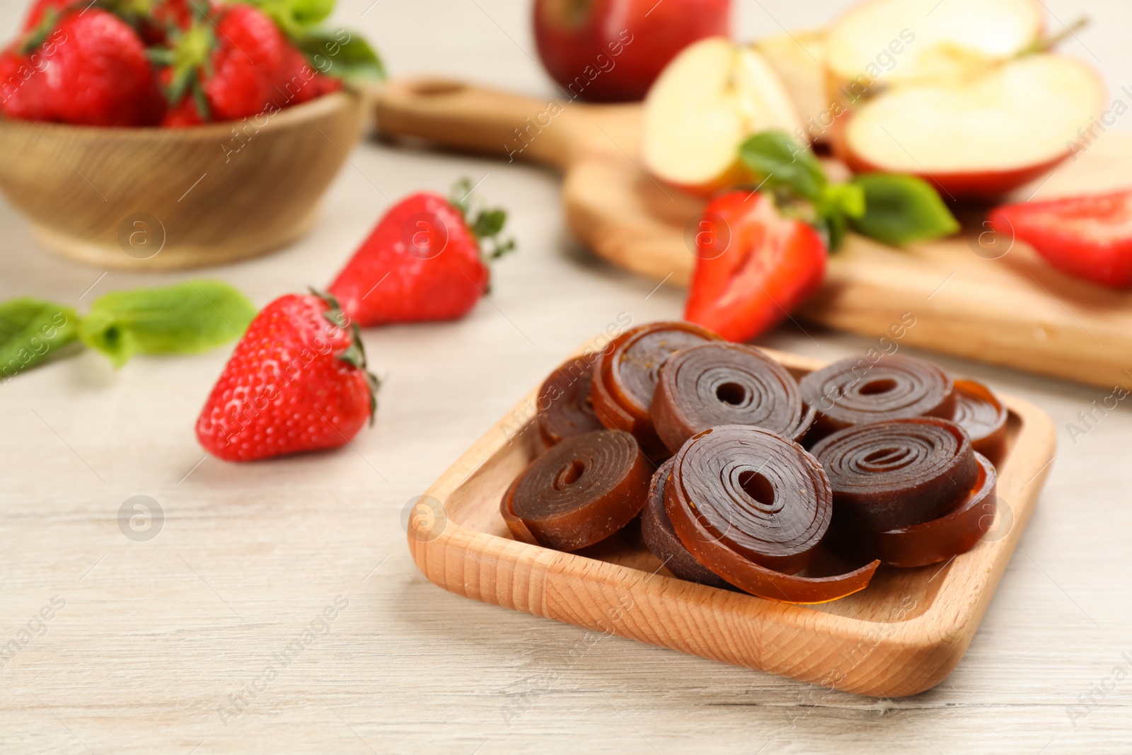 Photo of Composition with delicious fruit leather rolls on white wooden table. Space for text