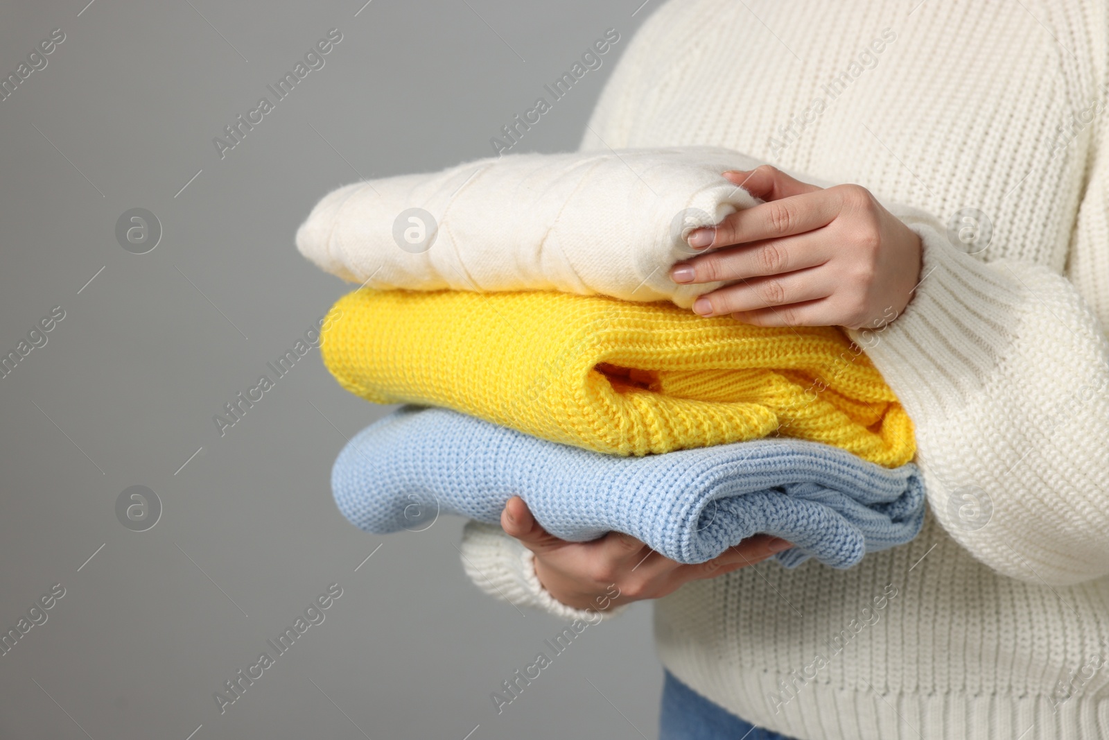 Photo of Woman with stack of knitted sweaters on grey background, closeup. Space for text