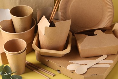 Eco friendly food packaging. Paper containers, tableware and eucalyptus leaves on pale yellow background, closeup