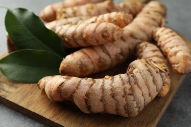 Photo of Many raw turmeric roots and green leaves on grey table, closeup