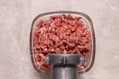 Manual meat grinder with beef mince on light grey table, top view