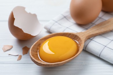 Photo of Spoon with raw egg yolk on white wooden table, closeup
