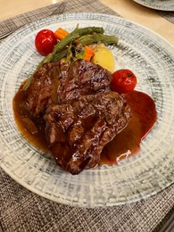 Photo of Delicious grilled beef steaks with sauce and vegetables served on table, closeup