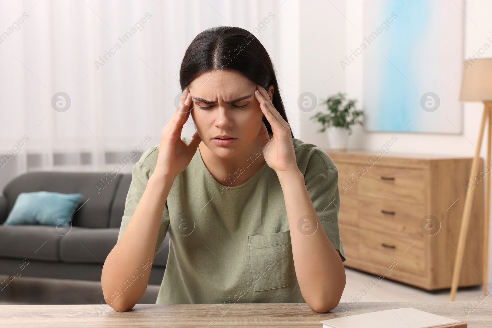 Photo of Sad woman suffering from headache at wooden table indoors