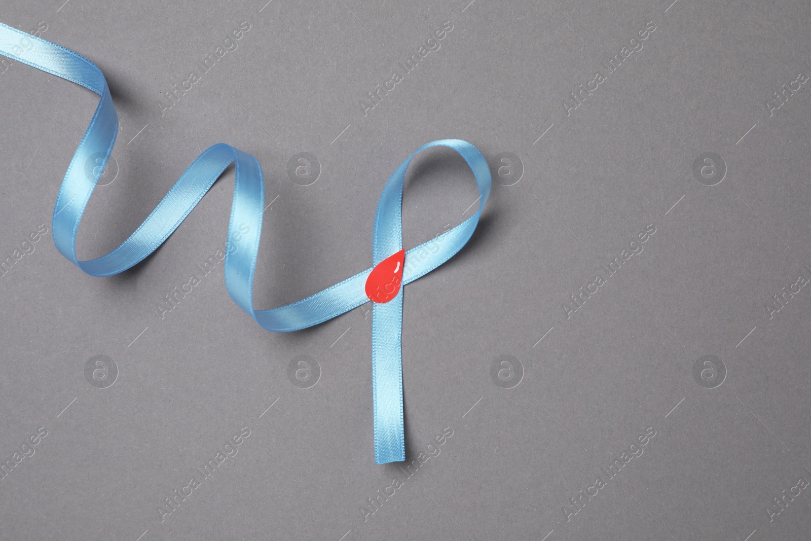 Photo of Light blue ribbon with paper blood drop on grey background, top view and space for text. Diabetes awareness