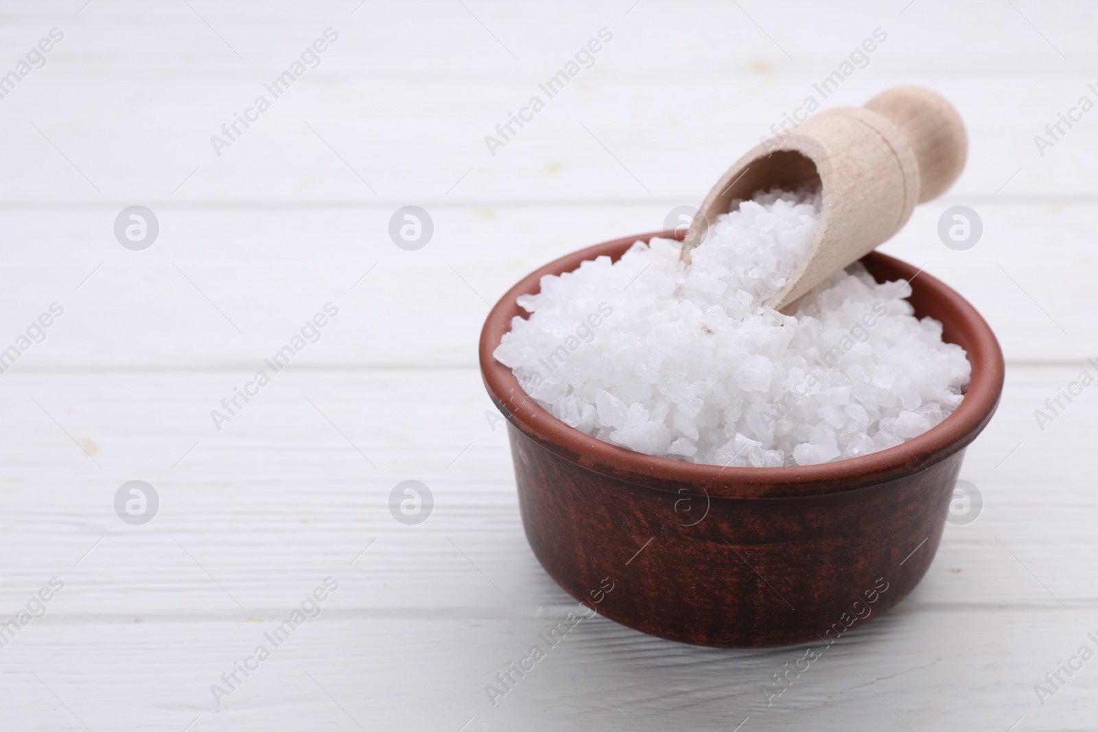 Photo of Bowl and scoop with sea salt on white wooden table, closeup. Space for text