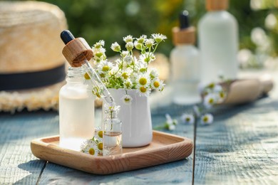 Photo of Bottles of chamomile essential oil, pipette and flowers on grey wooden table, space for text