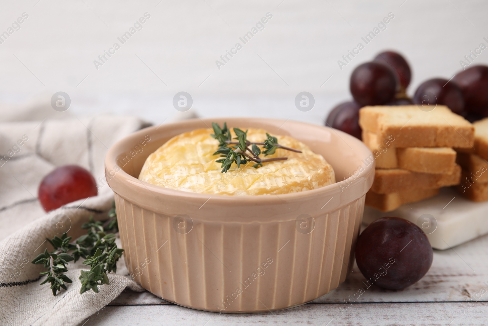 Photo of Tasty baked camembert in bowl, thyme, grapes and croutons on wooden table, closeup