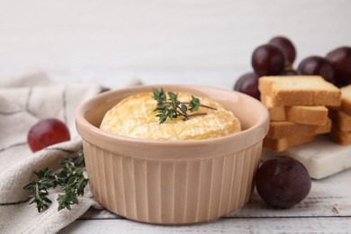 Tasty baked camembert in bowl, thyme, grapes and croutons on wooden table, closeup