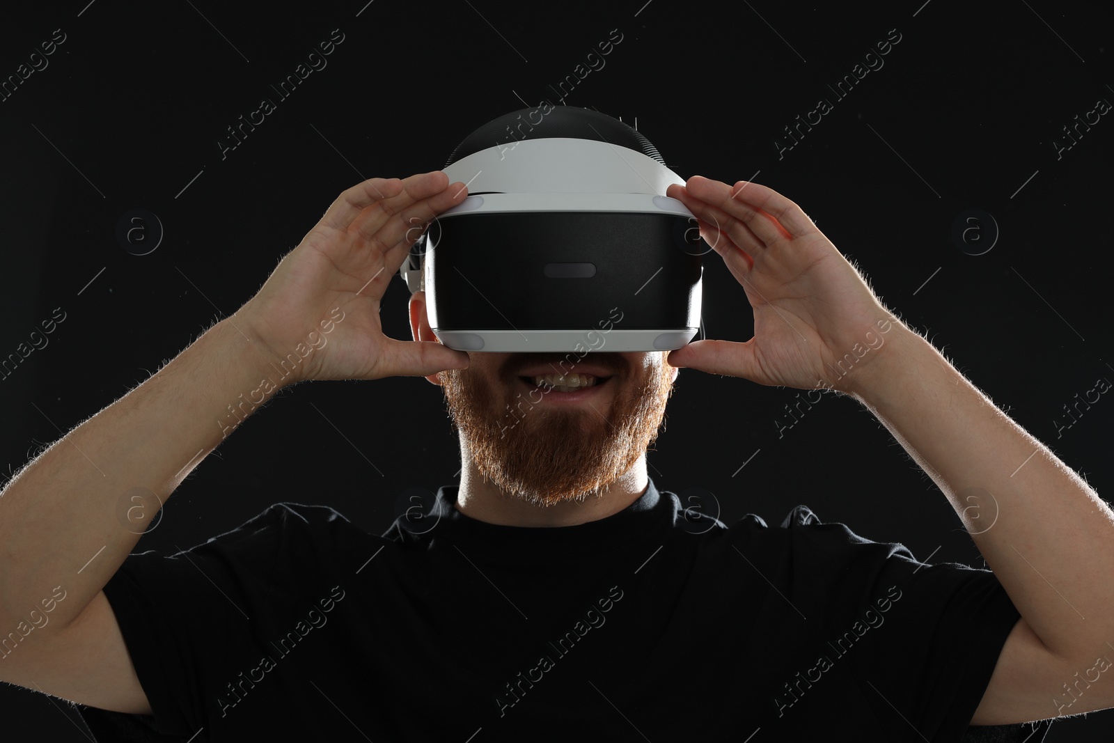 Photo of Smiling man using virtual reality headset on black background