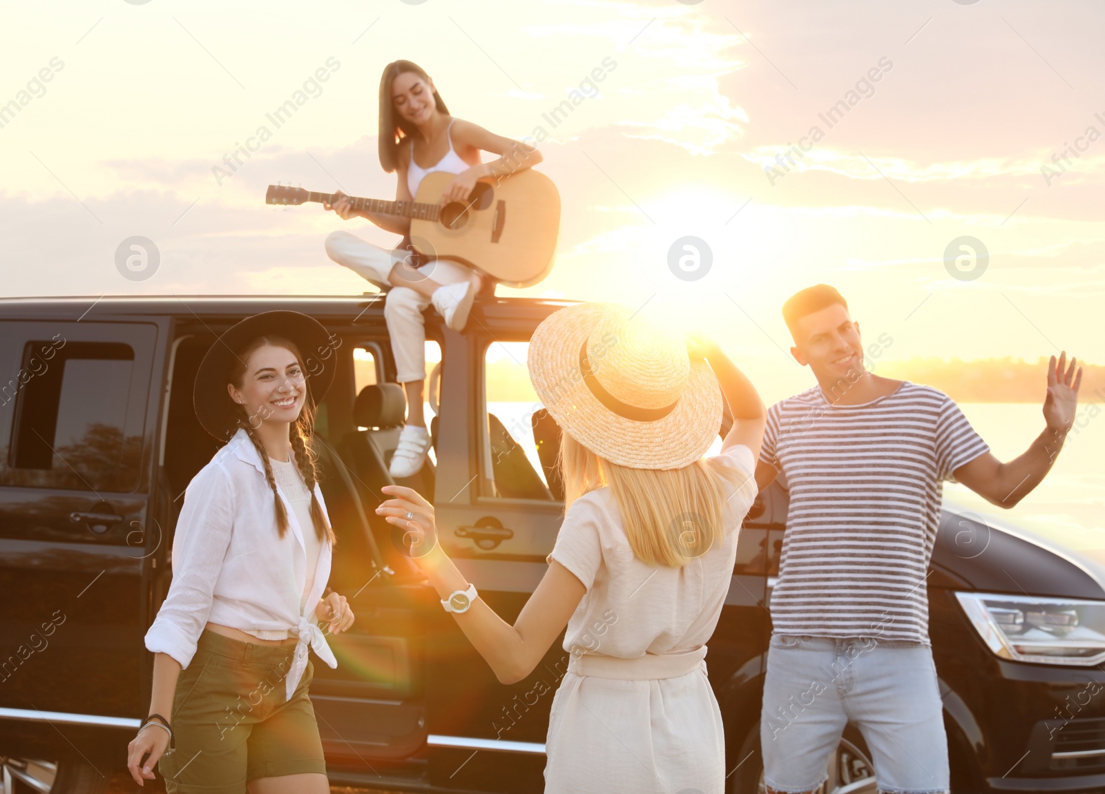 Photo of Happy friends having fun near car outdoors at sunset. Summer trip
