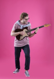 Young man playing electric guitar on color background