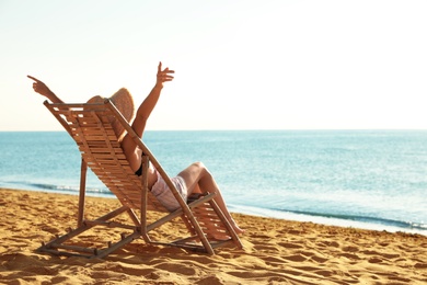 Photo of Woman relaxing on deck chair at sandy beach. Summer vacation