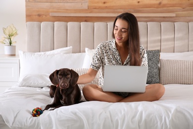 Young woman working on laptop near her dog in bedroom. Home office concept