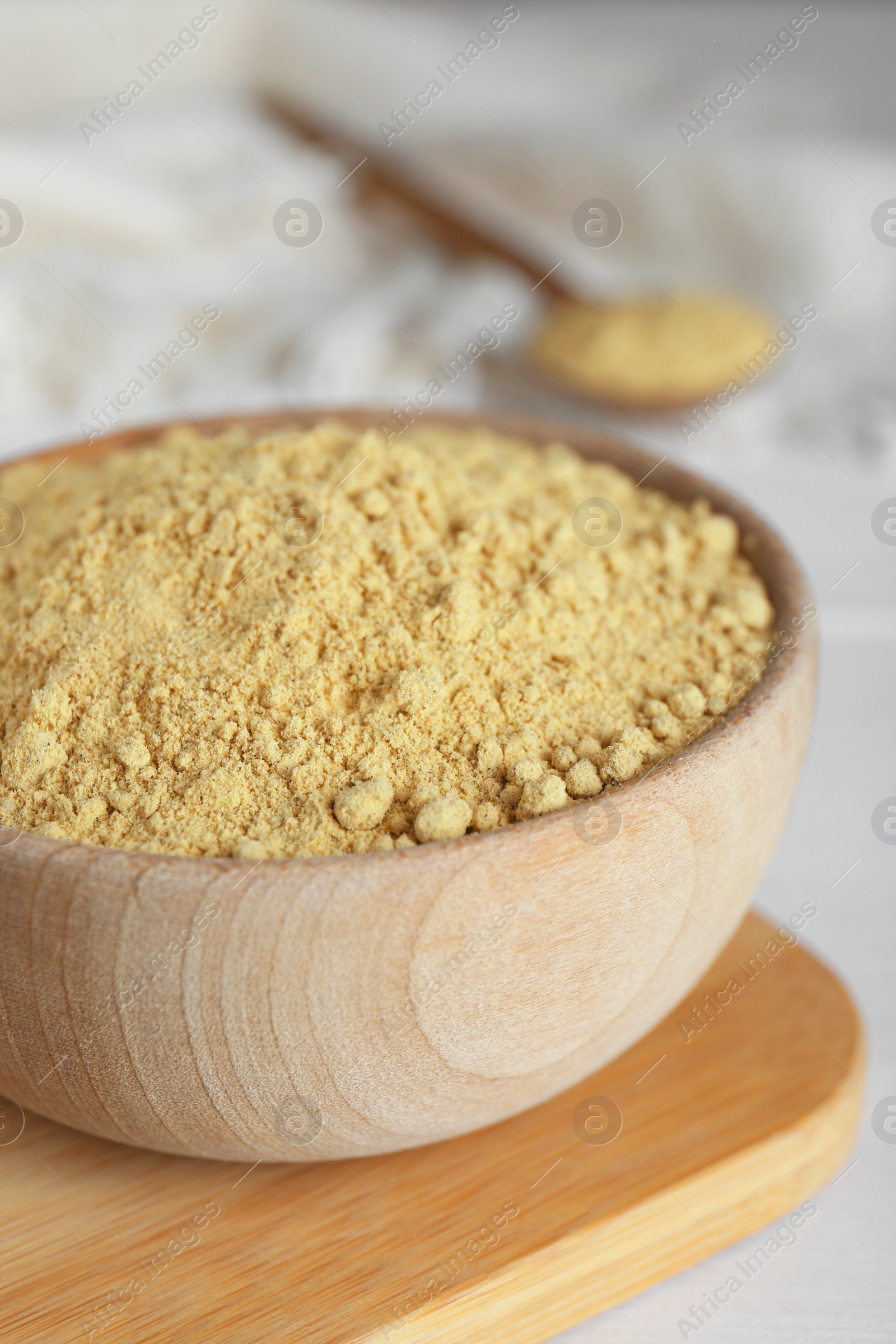 Photo of Bowl of aromatic mustard powder on white wooden table, closeup