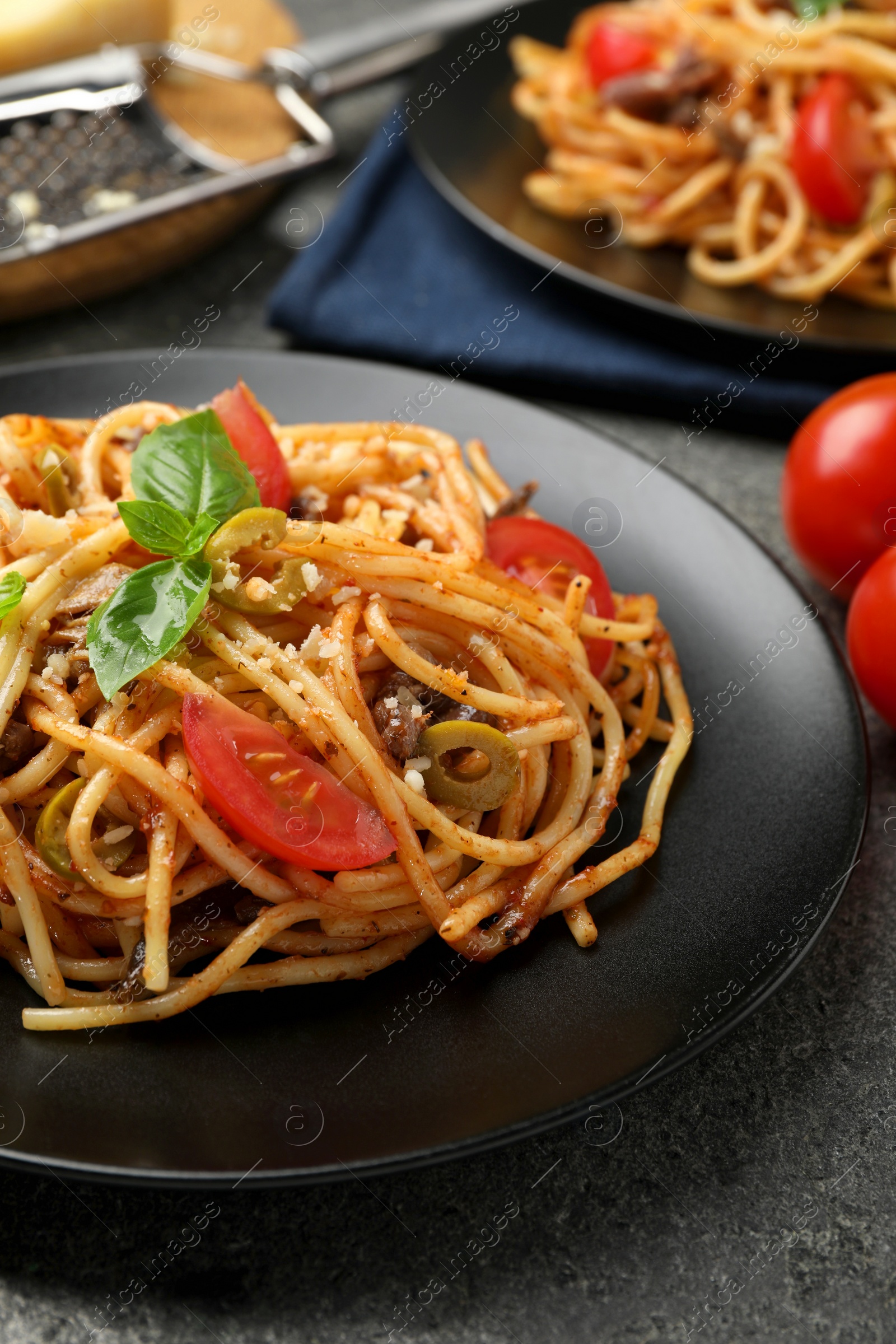 Photo of Delicious pasta with anchovies, tomatoes and olives on grey table