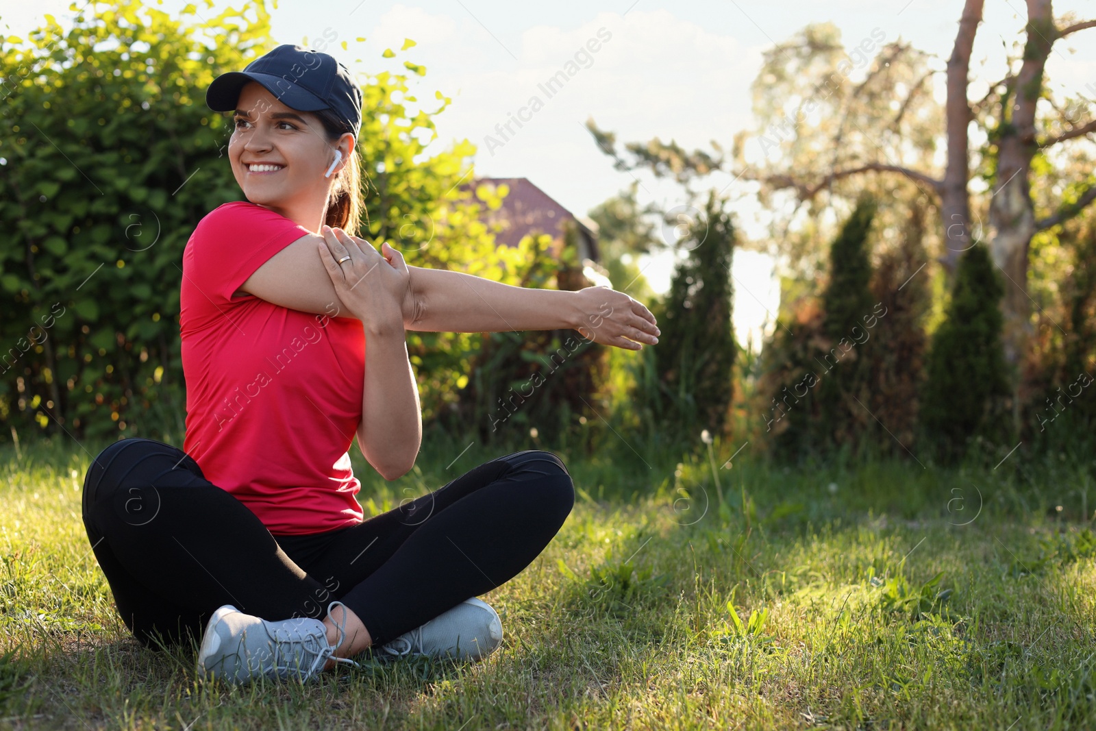 Photo of Young woman listening to music while doing morning exercise on green grass in park, space for text