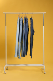 Photo of Rack with different jeans on yellow background