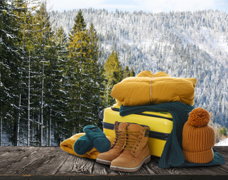 Image of Suitcase with warm clothes on wooden surface against beautiful winter landscape