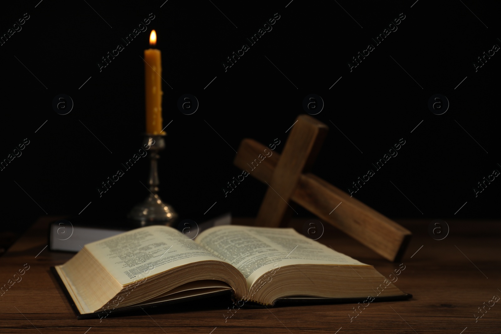 Photo of Church candle, Bible and cross on wooden table against black background