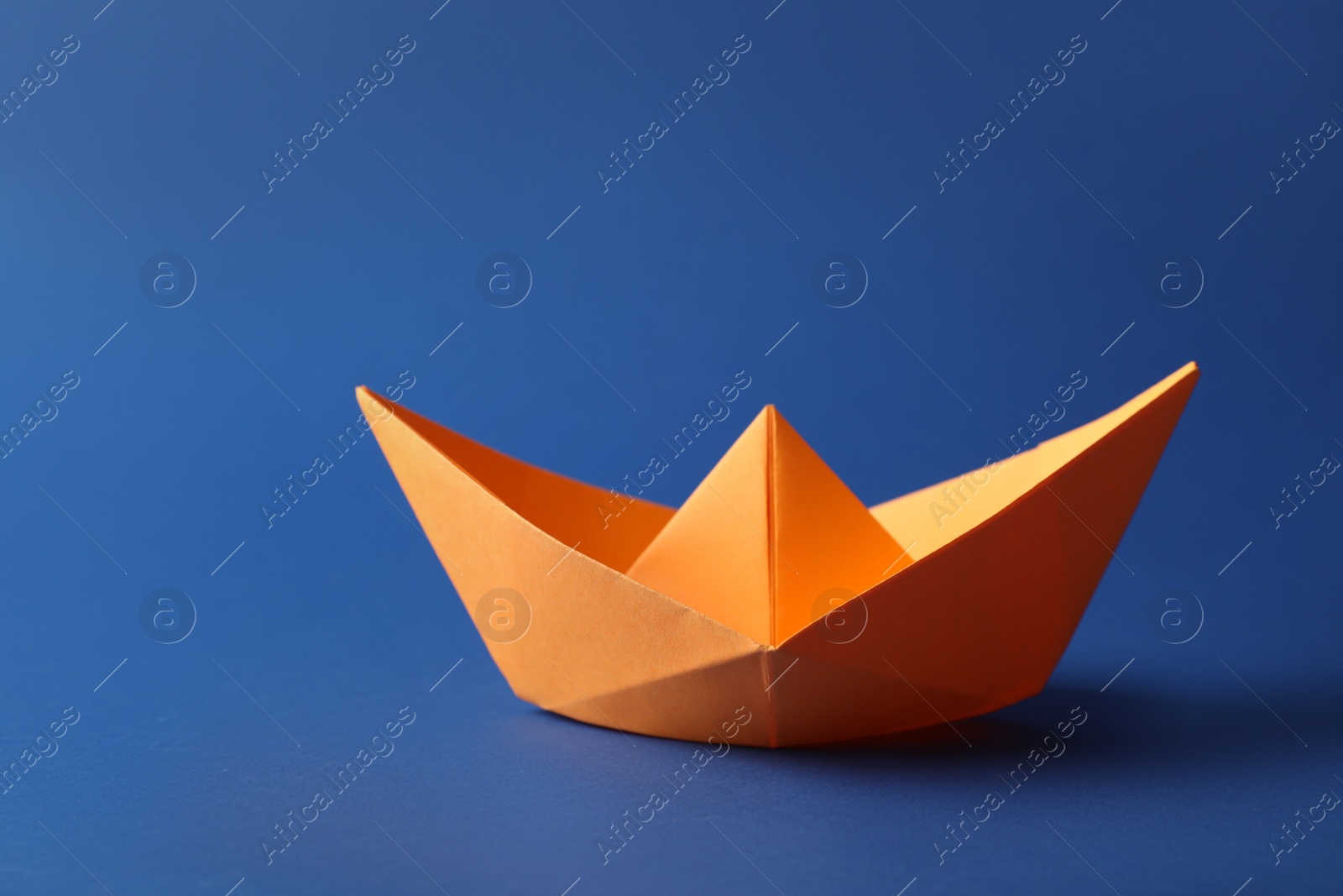 Photo of Handmade orange paper boat on blue background. Origami art