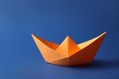 Handmade orange paper boat on blue background. Origami art