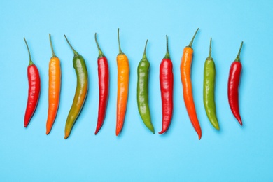 Photo of Different hot chili peppers on blue background, flat lay