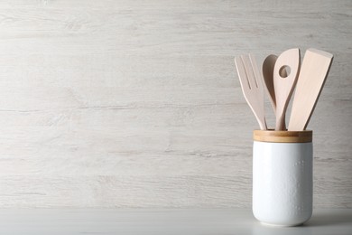 Photo of Holder with different kitchen utensils on white wooden table. Space for text